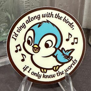 May include: A round sticker featuring a cartoon blue bird with a yellow beak and feet. The sticker has the text "I'd sing along with the birds, if I only knew the words" and musical notes around the bird.