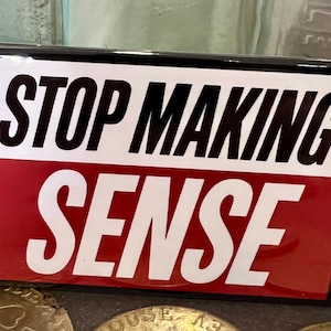 May include: A rectangular sticker with the words "STOP MAKING SENSE" in bold black letters on a white background, above the word "SENSE" in white letters on a red background. The sticker has a black border.