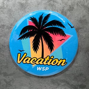 May include: A round button with a tropical vacation theme. The button features a black palm tree, a colorful sunset design, and the word "Vacation" in yellow script. Two birds are flying in the sky.