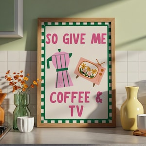 May include: A framed art print with a light beige background features a pink coffee maker and a retro TV with flowers. The text reads "SO GIVE ME COFFEE & TV" in pink. The frame is wood with a green and white border.