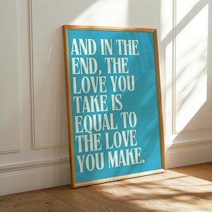 Könnte beinhalten: Ein gerahmtes Poster mit türkisfarbenem Hintergrund und dem Zitat "AND IN THE END, THE LOVE YOU TAKE IS EQUAL TO THE LOVE YOU MAKE" in weißem Text. Der Rahmen hat eine warme, hellbraune Farbe. Das Poster lehnt an einer weißen Wand.