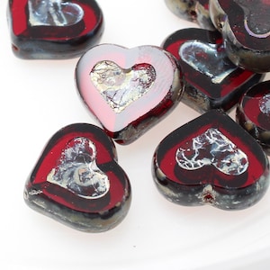 May include: A group of red glass heart-shaped beads with silver accents. The beads are scattered on a white surface.