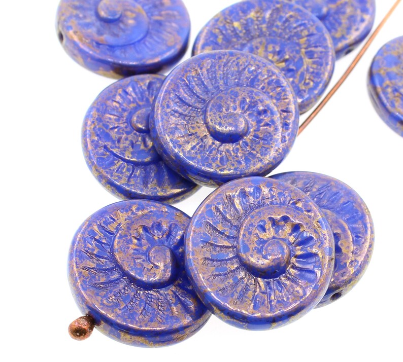 May include: A group of blue glass beads with a gold metallic finish. The beads are round and have a spiral design.
