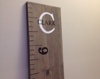 May include: A wooden growth chart with a white painted letter C and the name "CLARK" in black lettering. The chart has a ruler with black markings.