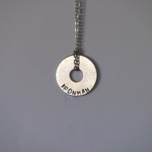 Peut inclure: Un collier en argent avec un pendentif rond sur lequel est inscrit "IRONMAN".
