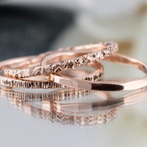 May include: Three rose gold stacking rings with textured surfaces. The rings are stacked on top of each other.