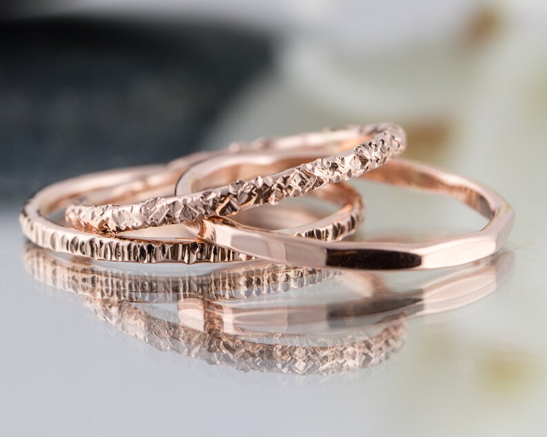 May include: Three rose gold stacking rings with textured surfaces. The rings are stacked on top of each other.
