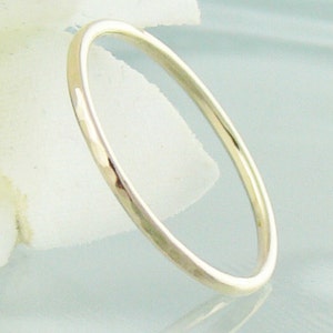 May include: A simple, thin silver band ring. The ring is smooth and has a slightly hammered texture.