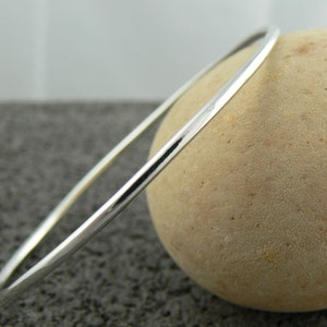 May include: A simple silver bangle bracelet, shown on a textured surface.