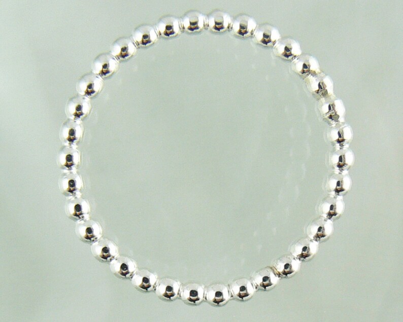 Puede incluir: Un brazalete de plata con un dise&ntilde;o sencillo. El brazalete est&aacute; hecho de peque&ntilde;as cuentas redondas que est&aacute;n espaciadas uniformemente.