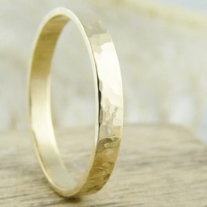 May include: A simple gold band wedding ring with a hammered finish.
