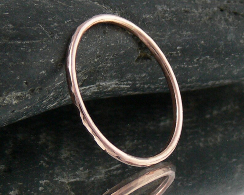 May include: A simple, hammered rose gold band ring. The ring is thin and delicate, with a smooth, polished finish.
