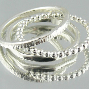 May include: Three silver rings stacked together. The top ring has a beaded design, the middle ring has a hammered texture, and the bottom ring is plain.