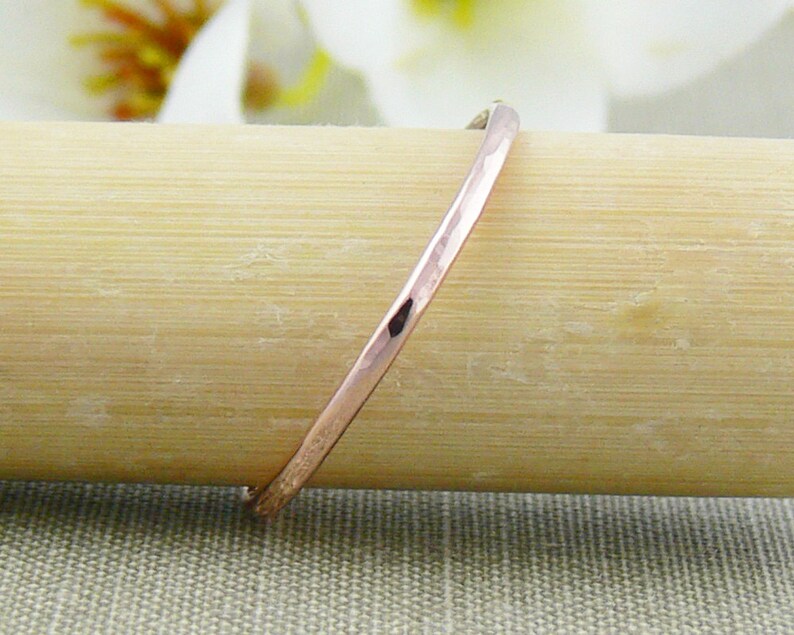 May include: A thin, hammered rose gold band ring. The ring is shown on a wooden surface.