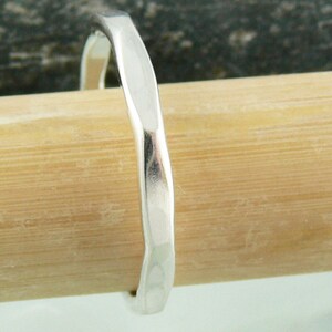 May include: A silver hammered ring with a smooth, rounded surface. The ring is shown on a wooden surface.