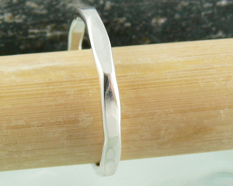 May include: A silver hammered ring with a smooth, rounded surface. The ring is shown on a wooden surface.