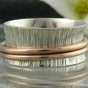 May include: A silver spinning ring with a rose gold band. The ring has a textured, vertical pattern.