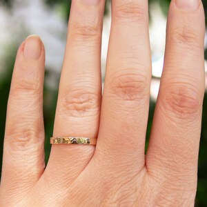 May include: A thin gold band ring with a hammered texture. The ring is worn on the ring finger of a hand.