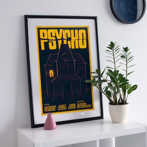 Puede incluir: Un póster enmarcado en negro con el título "Psicosis" en letras amarillas. El póster presenta una silueta oscura de una casa con una sola ventana iluminada. El póster también incluye los nombres de los actores y el director.
