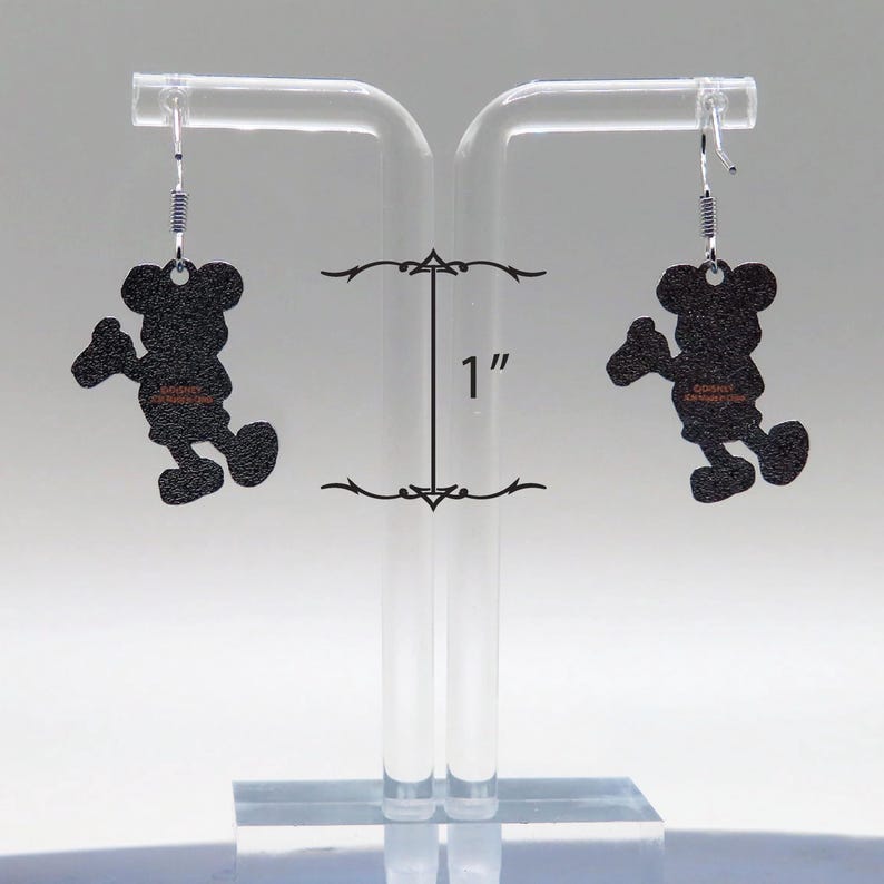 May include: A pair of black Mickey Mouse silhouette earrings. Each earring is approximately 1 inch in length. The earrings hang from silver-colored fish hook ear wires. The earrings are displayed on a clear acrylic earring stand.