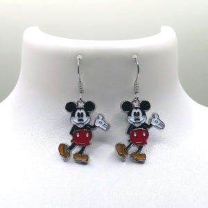 May include: A pair of dangle earrings featuring the iconic Mickey Mouse character. Each earring showcases a black and white Mickey Mouse with a red shorts, yellow shoes, and white gloves. The earrings are suspended from silver-colored fish hook ear wires.