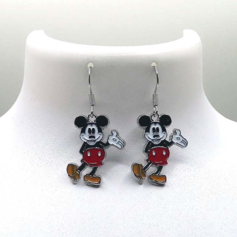May include: A pair of dangle earrings featuring the iconic Mickey Mouse character. Each earring showcases a black and white Mickey Mouse with a red shorts, yellow shoes, and white gloves. The earrings are suspended from silver-colored fish hook ear wires.