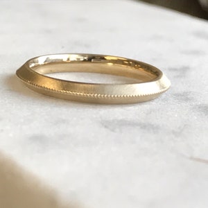 Op de afbeelding: Een eenvoudige gouden trouwring met een licht afgeronde rand en een getextureerd oppervlak.