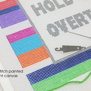 May include: Hand-painted canvas with the text "Hold on to everything" in gray. The canvas is 12 count and has a green, blue, orange, blue, pink, purple, and red striped border. A needle and green embroidery floss are on the canvas.