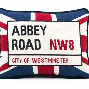 May include: A decorative pillow with a red, white, and blue Union Jack design. The pillow features a white rectangular patch with black text that reads "Abbey Road NW8 City of Westminster".