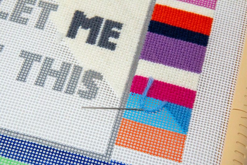 May include: A close-up of a needle and thread being used to stitch a colorful striped pattern on a white canvas. The text "LET ME DO THIS" is visible in the background.