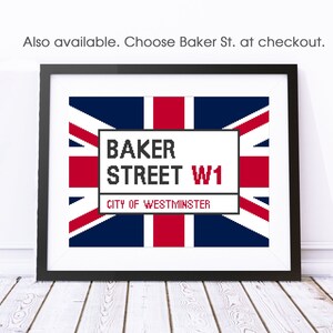 May include: A framed print of a white sign with the text "BAKER STREET W1 CITY OF WESTMINSTER" on a red, white, and blue Union Jack flag background.