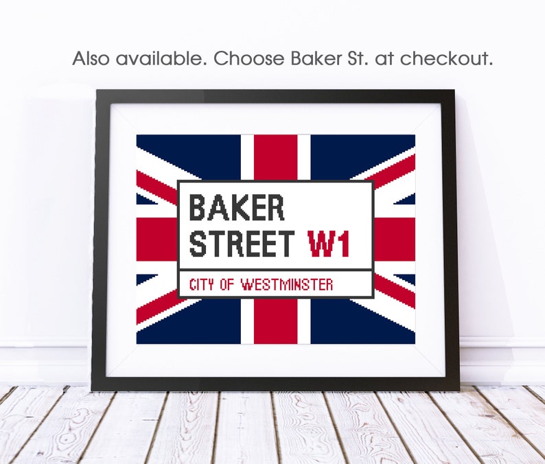 May include: A framed print of a white sign with the text "BAKER STREET W1 CITY OF WESTMINSTER" on a red, white, and blue Union Jack flag background.