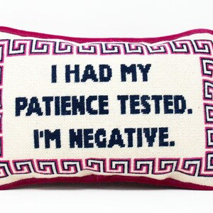 May include: A white pillow with a pink border and a blue Greek key design. The pillow has the text "I had my patience tested. I'm negative." embroidered on it.