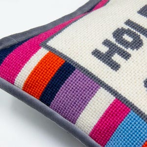 May include: A white pillow with a gray border and colorful stripes on the bottom. The pillow is embroidered with the text "Hold on" in gray.