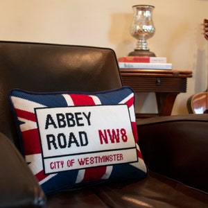 May include: A decorative pillow with a red, white, and blue Union Jack design. The pillow features a white rectangle with the text "Abbey Road NW8 City of Westminster" in black.