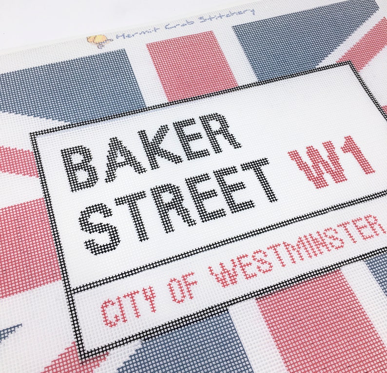 May include: A white canvas with a black frame and the text "BAKER STREET W1 CITY OF WESTMINSTER" printed in black. The canvas is decorated with a red, white, and blue Union Jack pattern.