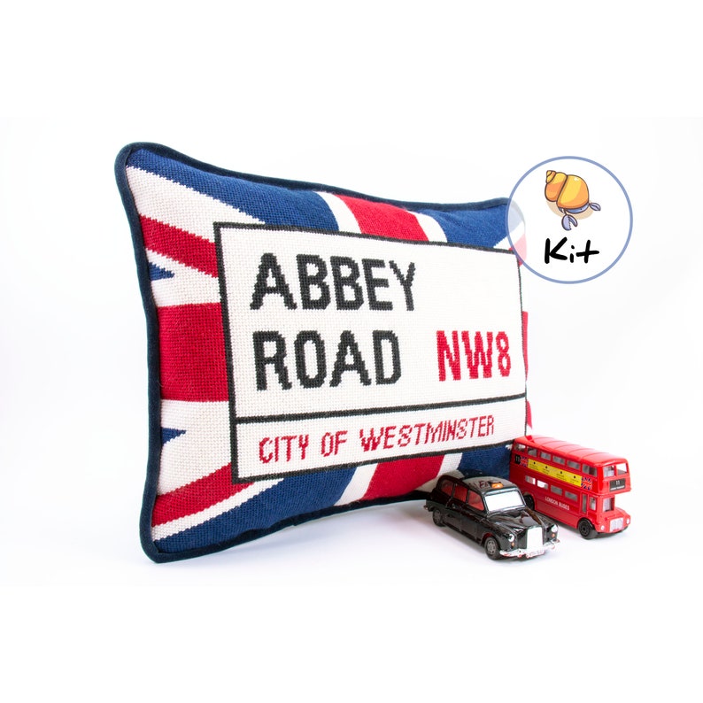 May include: A needlepoint pillow with a Union Jack design and a black and white sign that reads "Abbey Road NW8 City of Westminster".