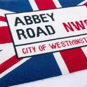 May include: A white sign with black text that reads "Abbey Road NW8 City of Westminster" on a red, white, and blue Union Jack background.