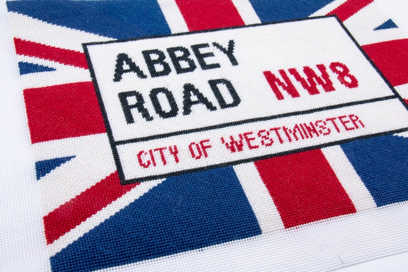 May include: A white sign with black text that reads "Abbey Road NW8 City of Westminster" on a red, white, and blue Union Jack background.