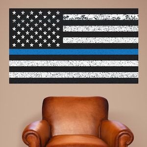 May include: A distressed American flag with a thin blue line running horizontally across the middle of the flag. The flag is displayed on a wall behind a brown leather armchair.