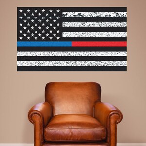 May include: A distressed American flag wall decal with a thin blue line and a red line, representing law enforcement and firefighters, displayed on a beige wall above a brown leather armchair.
