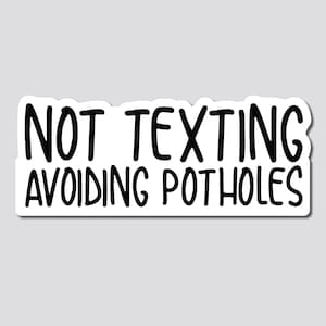 May include: White sticker with black text that reads "NOT TEXTING AVOIDING POTHOLES".