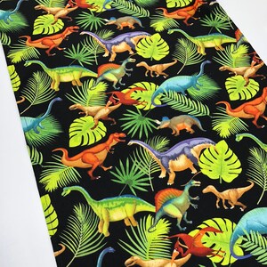 May include: Black fabric table runner with a repeating pattern of colorful dinosaurs and green tropical leaves.