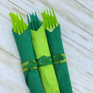 May include: Three green napkins with shamrock napkin rings. The napkins are folded and the rings are tied with green ribbon.