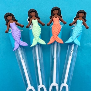 May include: Four mermaid-themed bubble wands with different colored mermaid tails: purple, green, orange, and blue. Each wand has a clear plastic tube with a bubble wand at the bottom.