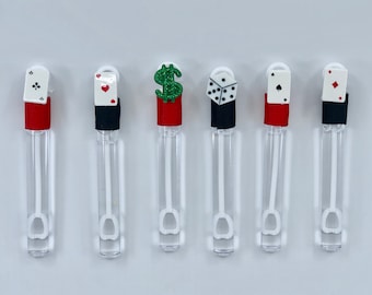 May include: Six clear plastic bubble wands with different casino-themed toppers. The toppers include a playing card with a spade, a playing card with a heart, a dollar sign, a die, a playing card with a club, and a playing card with a diamond.