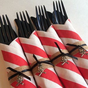 May include: Red and white striped napkins wrapped around black plastic forks with a silver skull and crossbones embellishment tied with twine and a black ribbon.