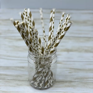 May include: A glass jar filled with gold and white striped paper straws with a pattern of small green trees.