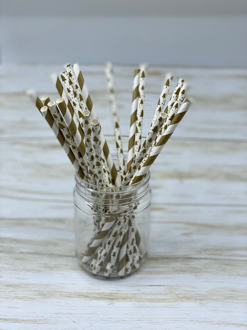 May include: A glass jar filled with gold and white striped paper straws with a pattern of small green trees.