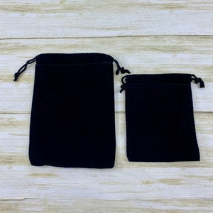 May include: Two black velvet drawstring pouches, one larger than the other, on a light wood surface.
